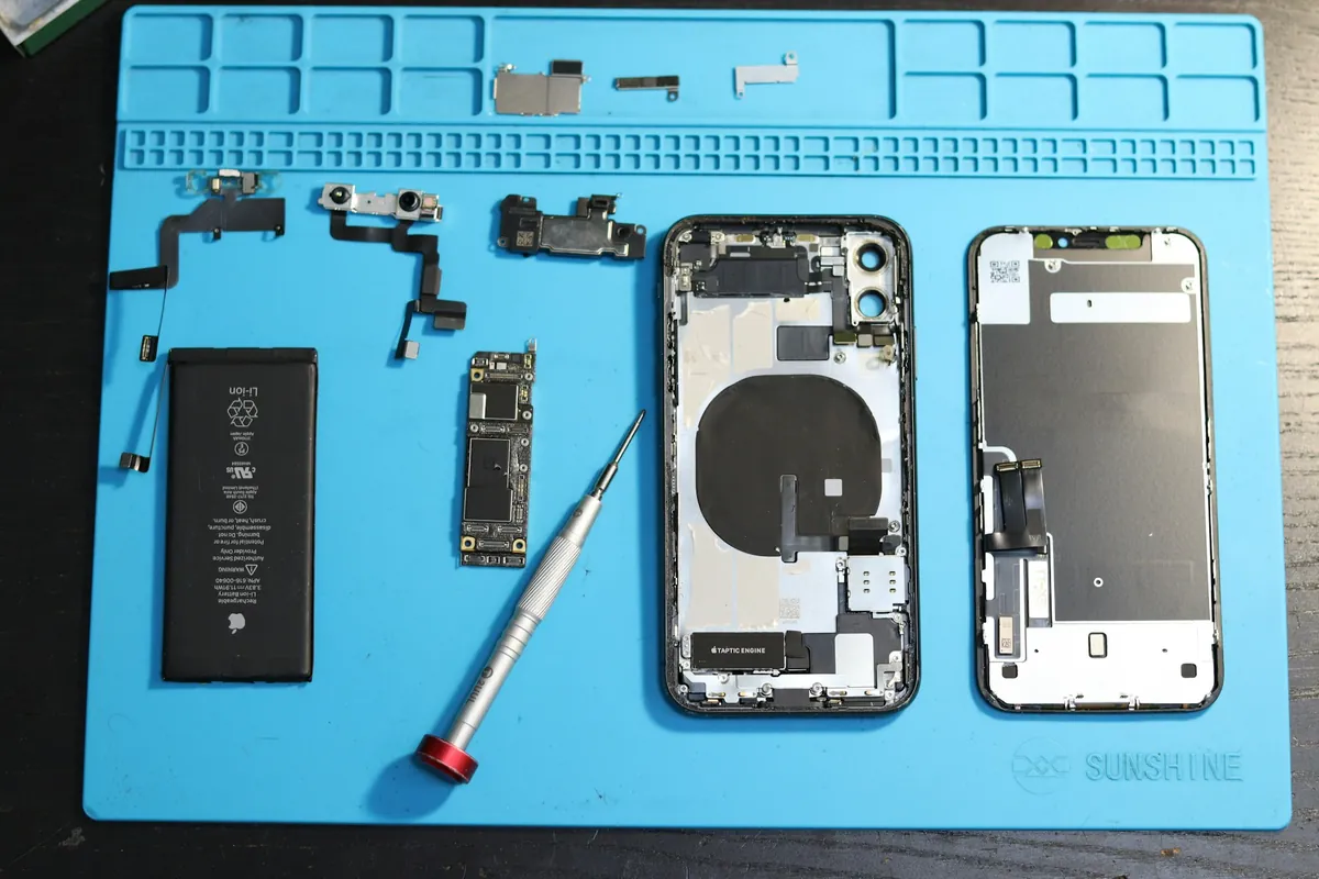 iPhone démonté sur un tapis d'atelier&nbsp;: batterie, écran et petites pièces