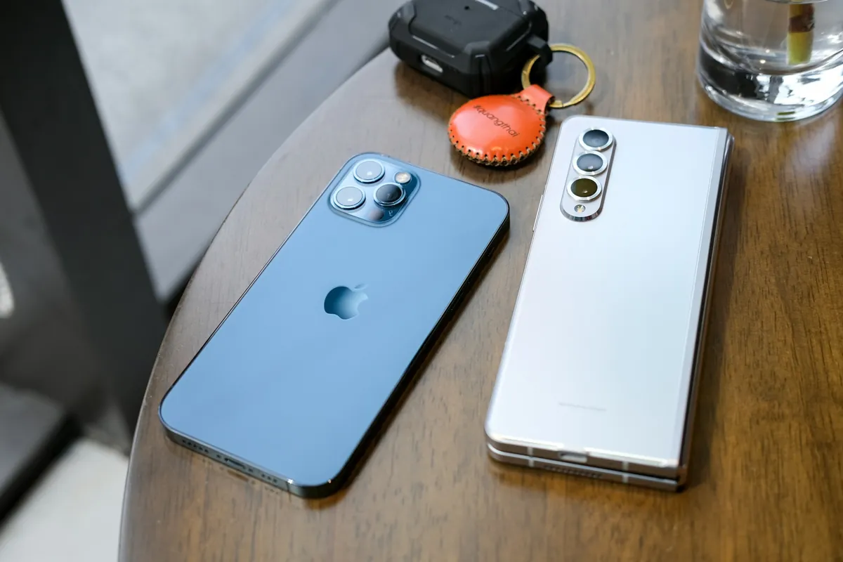 Un iPhone bleu et un Samsung pliable blanc posés sur une table en bois